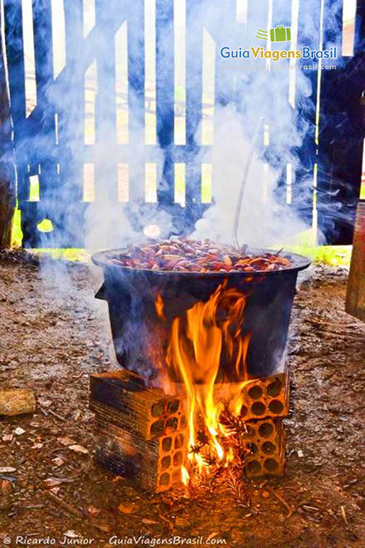 Imagem de uma panela de ferro com pinhão no fogo para cozinhar.